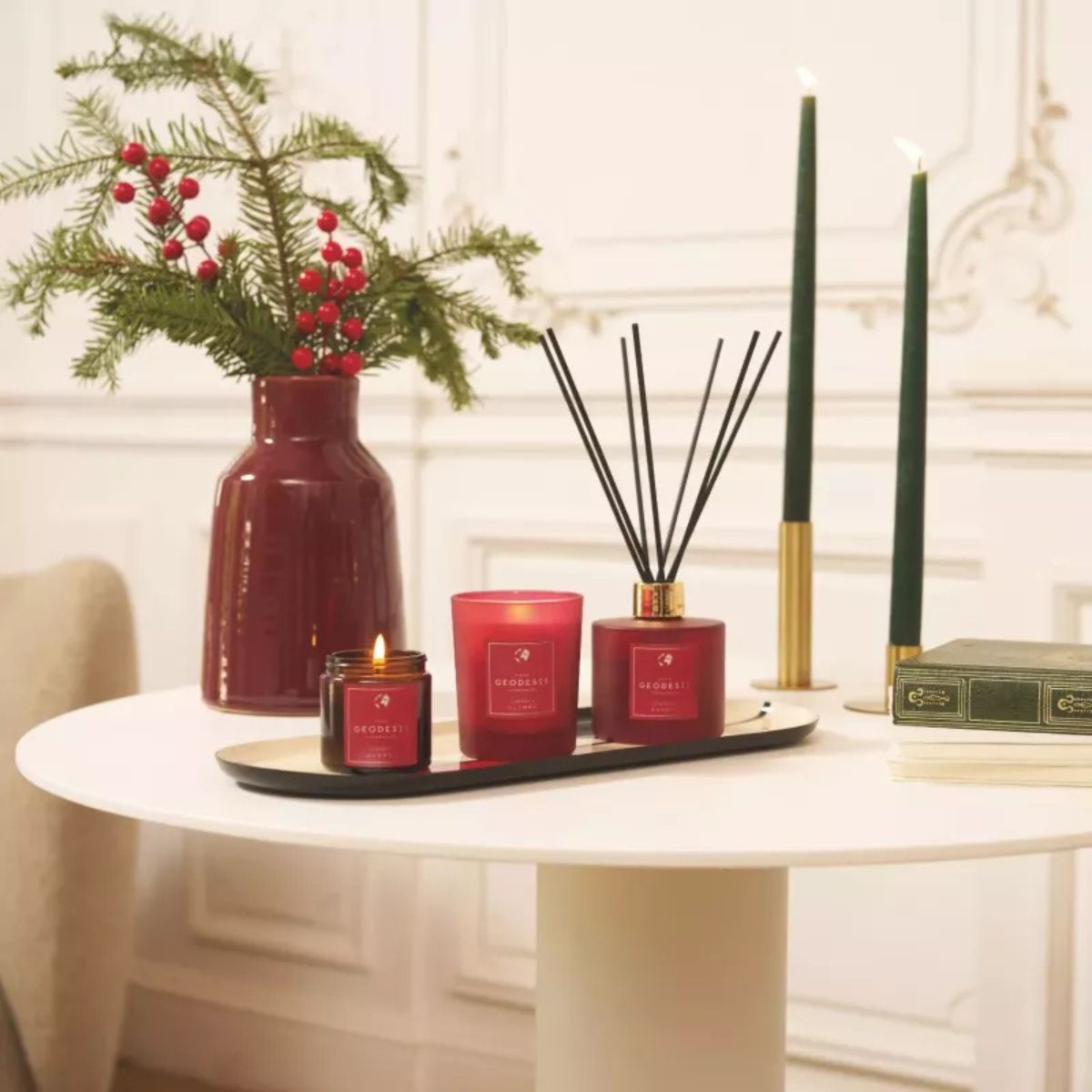 Collezione Geodesis Cranberry con diffusore, candela e spray ambiente su tavolino, accanto a fiori e decorazioni natalizie.